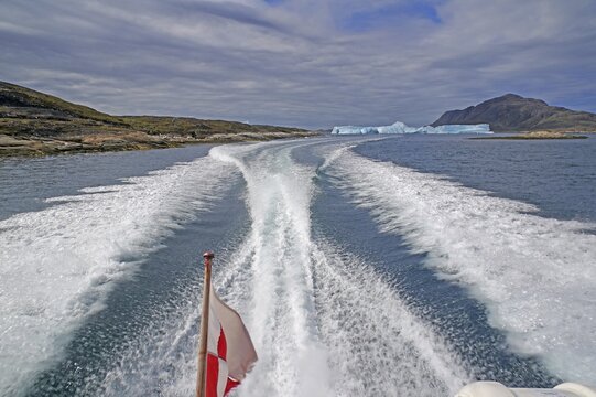 Boat passing icebergs in a fjord, Greenlandic flag, Qaqortoq, Greenland, Denmark