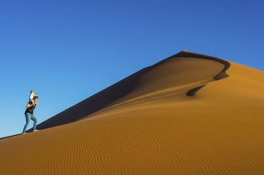 Woman with her baby walking up the giant sanddune Dune 45, Namib-Naukluft National Park, Namibia