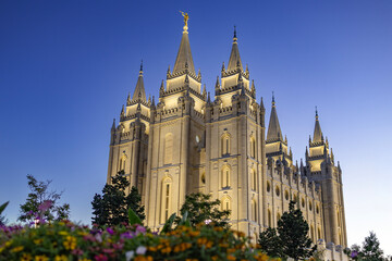 Obraz premium Salt Lake Temple at sunset, beautifully illuminated against a colorful evening sky, showcasing the iconic granite architecture, distinctive towers, and peaceful grounds of this historic Latter-day Sai