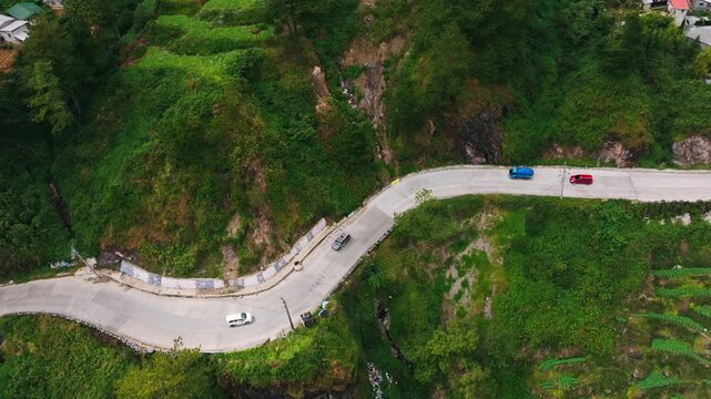 Vehicles follow a winding mountain highway through lush green Atok, Benguet