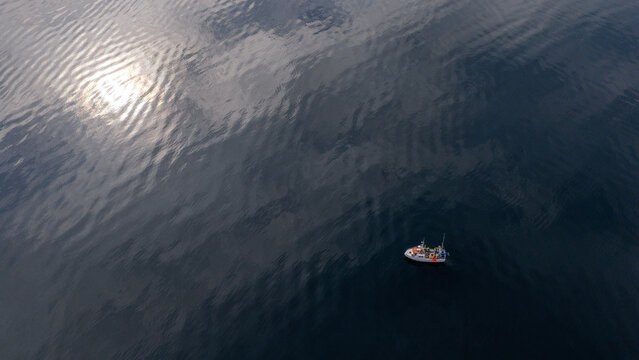 Aerial view of a small boat floating on the dark, calm waters of a fjord with sunlight reflecting on the surface in Liabygda, More og Romsdal, Norway.