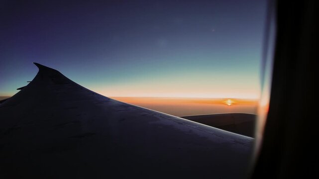 Dark airplane wing silhouette against a bright sunrise seen from a passenger window.
