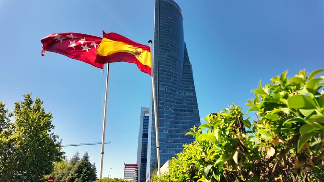 Low angle view of Madrid and Spanish flags flying in front of Torre de Cristal and modern office towers in Madrid.