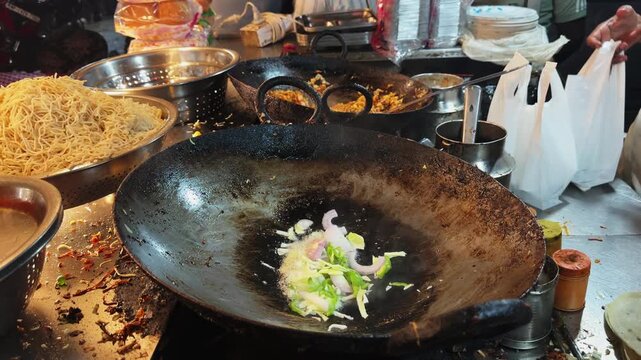 Fresh onion and green capsicum sizzling in hot oil inside a large iron wok during preparation of Indo Chinese street food