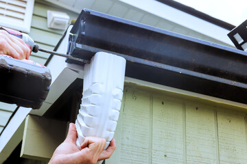 Obraz premium Worker works on attaching section of gutter to house takes place in residential area
