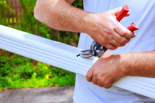 Worker uses sharp shears to cut piece of gutter metal pipe in garden area