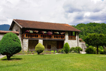 A traditional stone residential building adorned with a wooden flower-lined balcony stands within landscaped monastery grounds in Montenegro © Gregory
