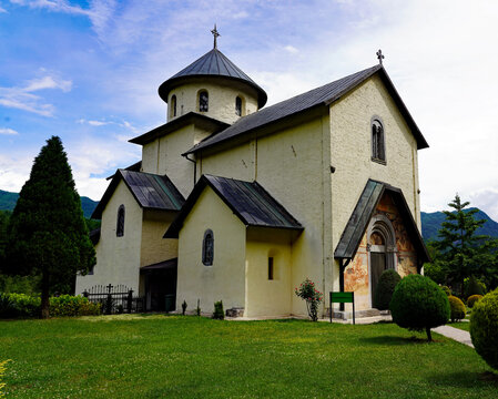 The historic Morača Monastery church stands surrounded by manicured green lawns and landscaped gardens against a mountainous backdrop in Montenegro