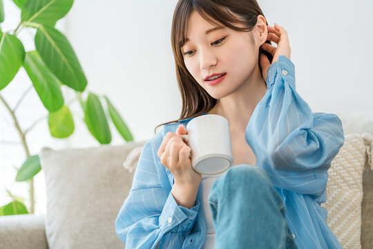 自宅のソファでコーヒー,ホットドリンクを飲みながらくつろぐ女性