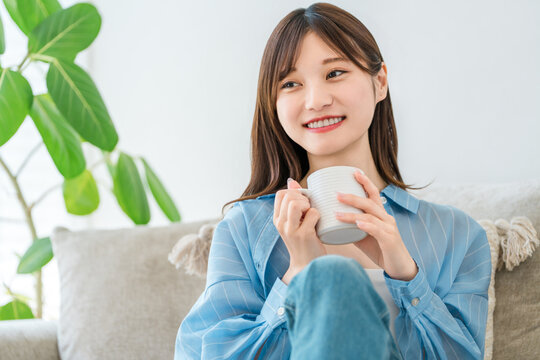 A woman relaxing on her sofa at home, sipping coffee and a hot drink.