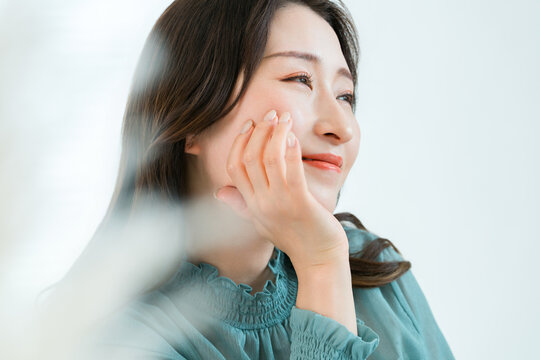 A woman touches her cheek and smiles, an image of skincare and beauty that reflects satisfaction with beautiful skin.