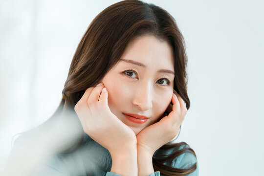 A woman touches her cheek and smiles, an image of skincare and beauty that reflects satisfaction with beautiful skin.