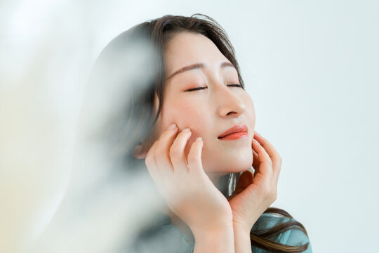 A woman with her eyes closed touching her cheek; beautiful skin, skincare, self-care image.