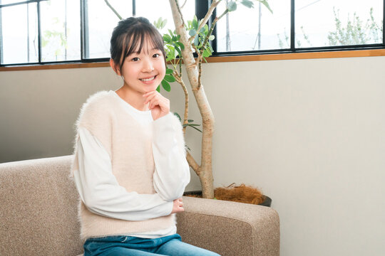 A smiling girl sitting on the sofa in her home (thinking, having an idea, imagining)