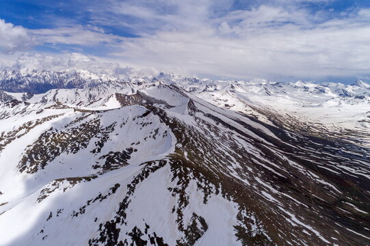 Aerial view of Babusar Top, showing snow-capped mountain peaks, rugged terrain, and dramatic ridges under a blue sky with scattered clouds in Naran, Khyber Pakhtunkhwa, Pakistan.