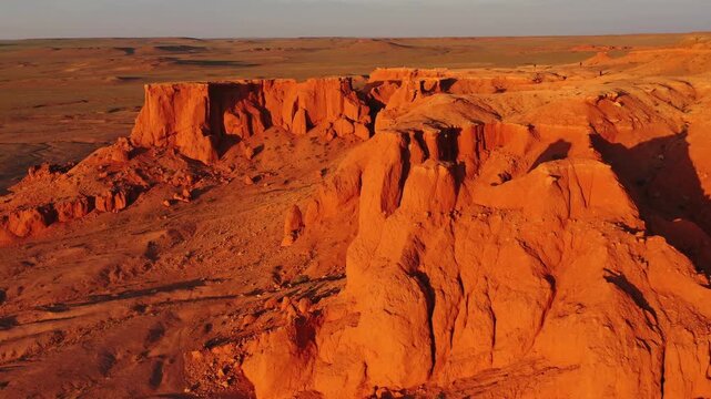 Aerial view of Flaming Cliffs in the Gobi Desert with orange sandstone formations under golden hour light, Bulgan, Omnogovi, Mongolia.