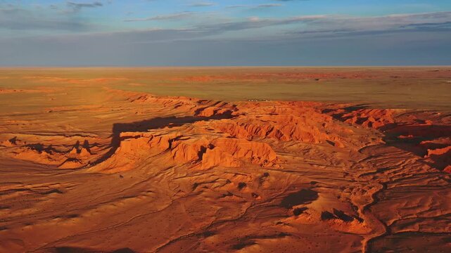 Aerial view of the red sandstone Flaming Cliffs in the Gobi Desert with vast arid landscape under golden hour light in Bulgan, Omnogovi, Mongolia.
