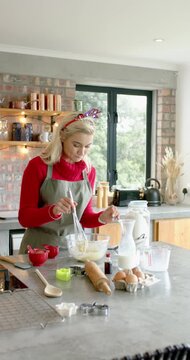 Vertical video: Woman whisking batter at counter with glass bowl and whisk for Christmas cookies