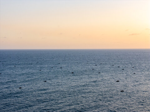 Aerial view of numerous small fishing boats scattered across the calm ocean surface during a golden sunset in Pacitan, East Java, Indonesia.
