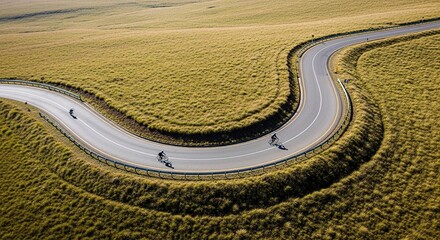Obraz premium Aerial view of cyclists riding along a winding road through a vast rural landscape.