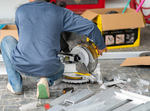 Construction worker using a electric circular miter saw to precisely cut aluminium profiles on a outdoor job site.