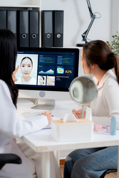Young asian woman doctor consulting with woman patient in aesthetic clinic during looking at computer screen artificial intelligence software for beauty facial skin analysis diagnostic result.