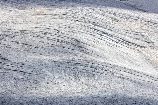 View of the textured ice surface and crevasses of the Ghiacciaio del Rutor in La Thuile, Aosta Valley, Italy.
