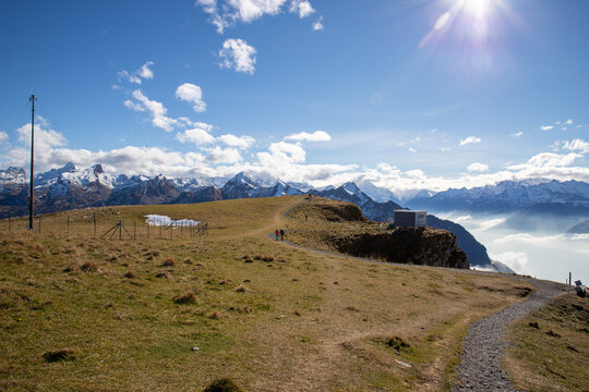 View of the Stoos mountain landscape with a hiking path, snow-capped peaks, and a clear blue sky in Morschach, Schwyz, Switzerland.