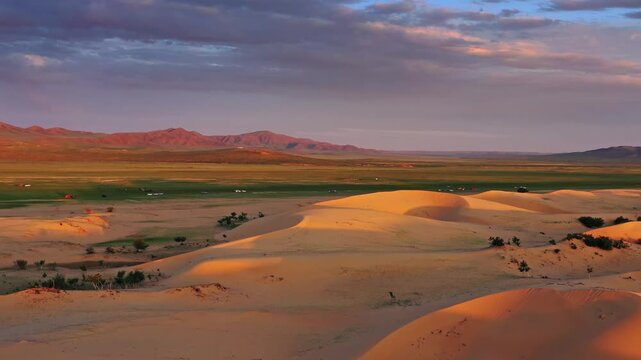 Aerial view of Elsen Tasarkhai sand dunes at golden hour with grassy plains and distant mountains in Hogono Taranaiin Huree, Bulgan, Mongolia.