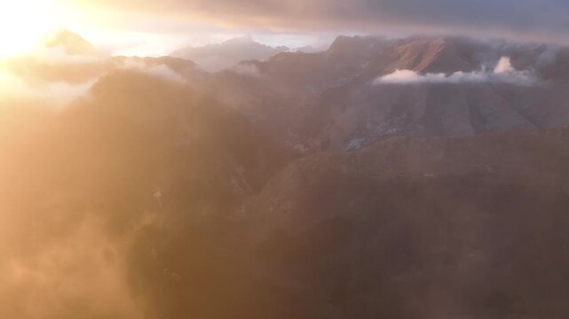 Aerial view of Monte Corchia peaks emerging through golden clouds at sunset in Stazzema, Tuscany, Italy.