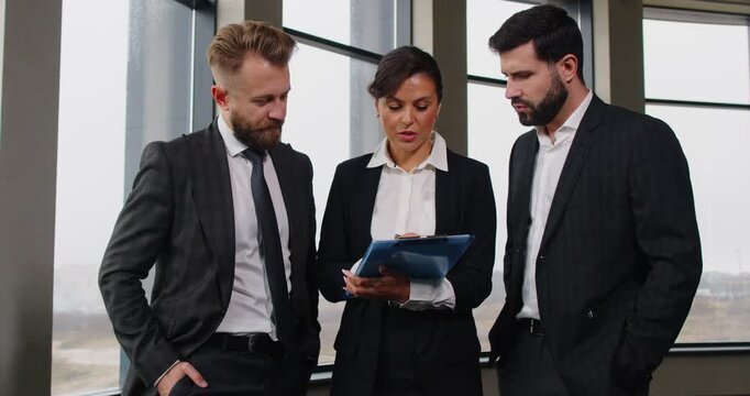 Three engaged diverse managers in formal suit discussing business project, talking in office, female boss, manager training new employees, leadership teamwork speaking looking at paper documents