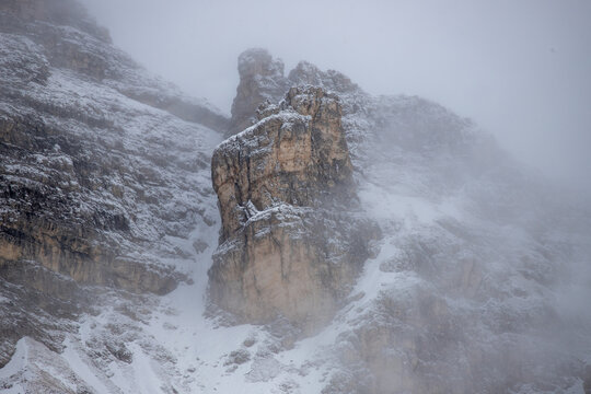 View of the snow-covered rocky peaks of the Dolomites shrouded in thick fog and mist in the mountains of Veneto, Italy.