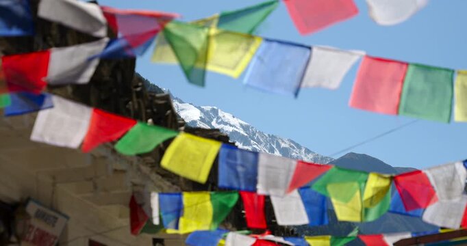Marpha Village, Mustang Nepal, low-angle shot looking up at colorful Tibetan prayer flags stretched across traditional whitewashed stone houses under a clear Himalayan sky.