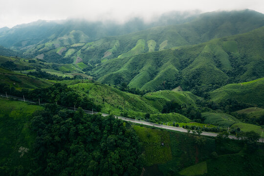 Aerial view of a winding asphalt road cutting through lush green mountains and tropical rainforest.