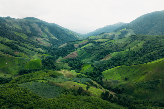 Aerial view of lush green rolling hills and agricultural valleys in a tropical mountain landscape.