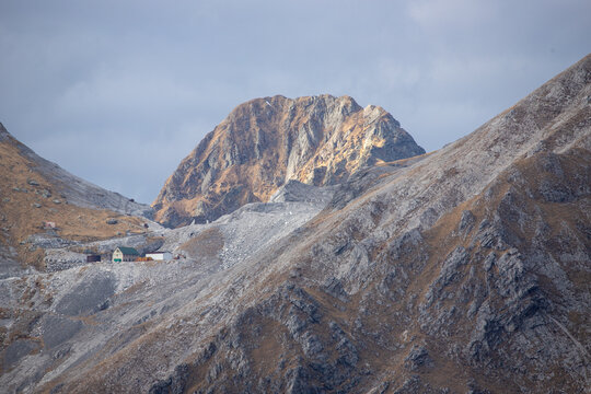 View of the Apuan Alps featuring rugged rocky peaks, steep slopes, and a small industrial quarry facility in the mountainside in Minucciano, Tuscany, Italy.