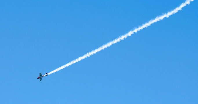 Aerobatic Stunt Plane Performing Maneuvers with Smoke Trail in Blue Sky