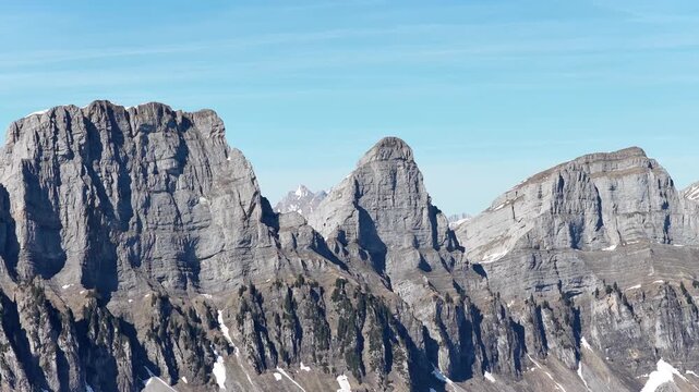 Aerial view of the dramatic Churfirsten mountain range above Walensee near Walenstadt, Switzerland, showcasing rugged limestone peaks, forests and clear alpine skies.