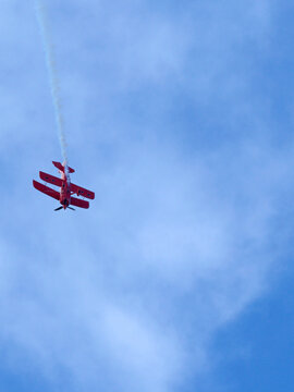 Red Biplane Performing Aerobatic Maneuvers with Smoke Trail in Blue Sky