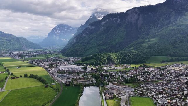 Niederurnen Switzerland aerial droen view of river town valley mountain forest landscape Glarus alpine alps, drone pushes forward flies over.