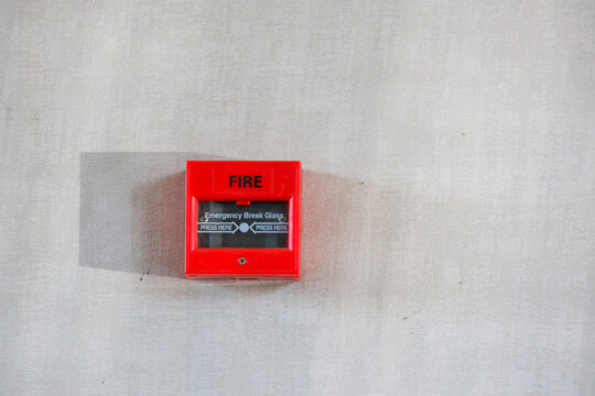Red fire alarm mounted on a plain wall. Clear instructions visible on the panel's glass. Emergency alert device ready for quick use. Ideal for safety signage or building interiors