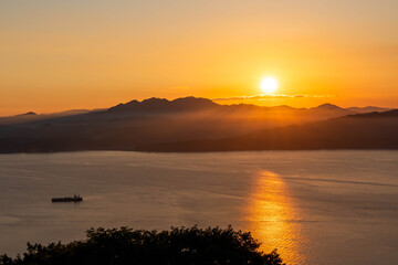 Fototapeta premium Sunset into Distant Hazy Mountains, Reflecting on the Sea
