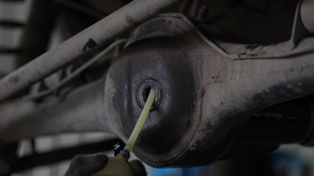 Dusty underbody view of car axle differential housing fill hole.