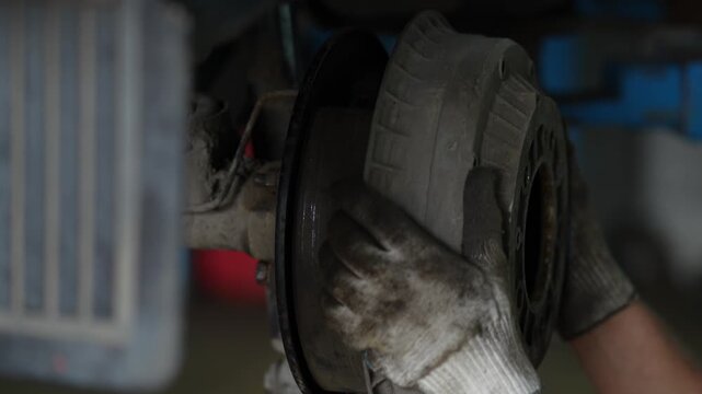 Gloved hand installs a dirty metal brake drum onto hub.