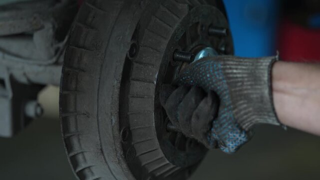Gloved hand installs a dirty metal brake drum onto hub.