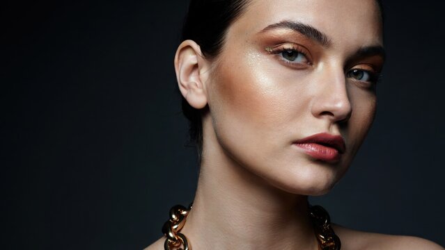 Elegant woman with bronze makeup and gold chain necklace, high fashion beauty portrait with glowing skin, luxury jewelry editorial
