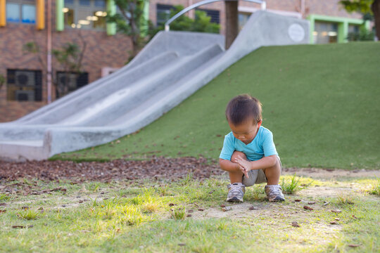 Toddler squatting on ground near playground slide outdoors