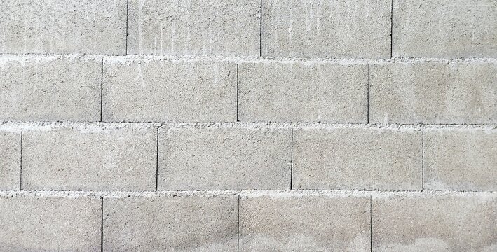 Front view of a wall constructed from standard concrete masonry units, stacked in rows, displaying the raw, rough, and natural grey texture of mortar and sand. Ideal for use as a background.
