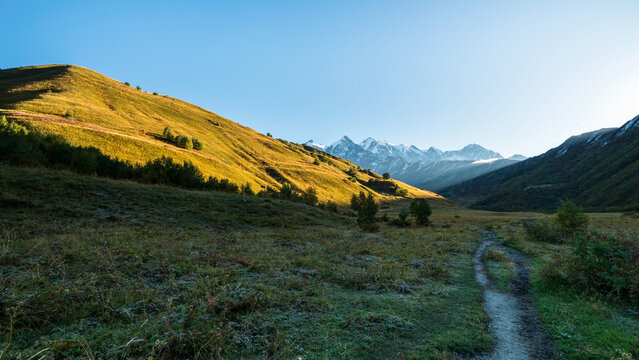 Landscape photograph of hiking trail beyond Adishi village toward Adishi Pass with morning light on autumn mountains in Svaneti Georgia.