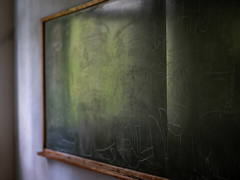 Close-up of an old green classroom chalkboard covered with faded children's drawings, scribbles and handwritten notes in a disused rural school.